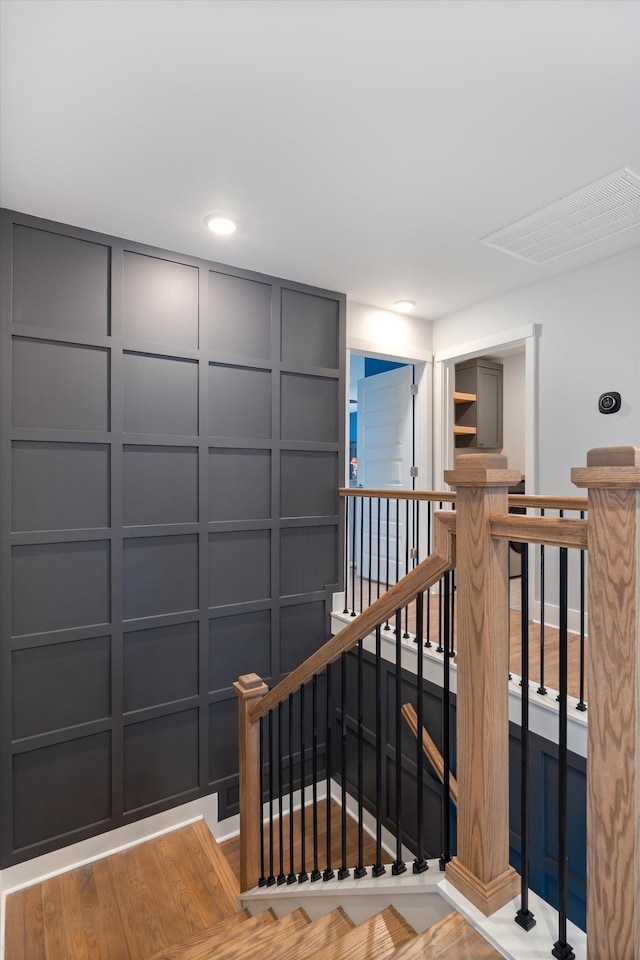 stairway featuring a decorative wall, recessed lighting, wood finished floors, and visible vents
