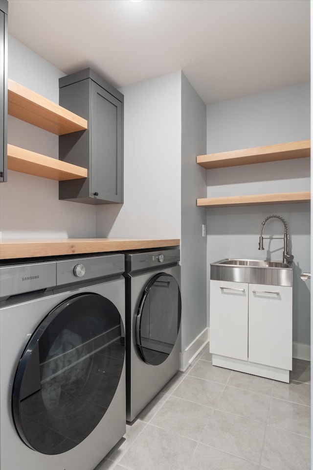 washroom with a sink, cabinet space, separate washer and dryer, light tile patterned floors, and baseboards