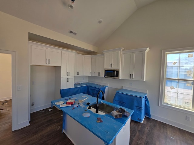 kitchen featuring visible vents, a center island with sink, a sink, white cabinets, and stainless steel microwave