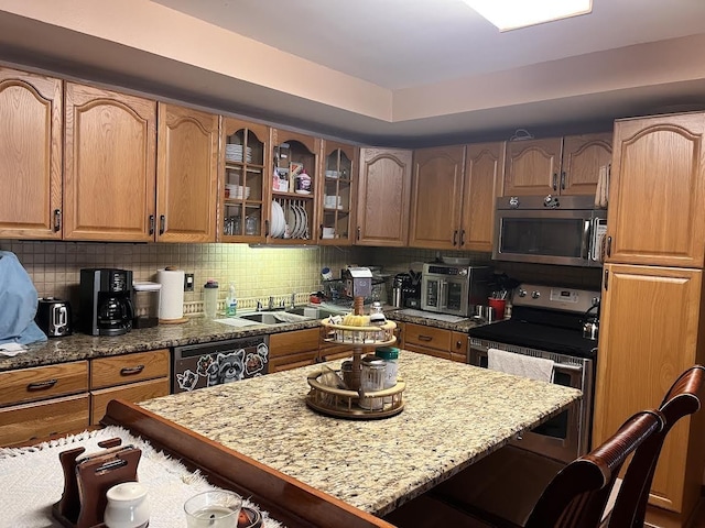 kitchen featuring appliances with stainless steel finishes, a breakfast bar area, light stone countertops, backsplash, and glass insert cabinets