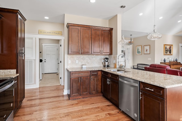kitchen featuring a peninsula, backsplash, stainless steel appliances, light wood finished floors, and a sink