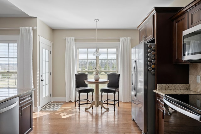 kitchen featuring dark brown cabinetry, light wood-style flooring, tasteful backsplash, stainless steel appliances, and decorative light fixtures