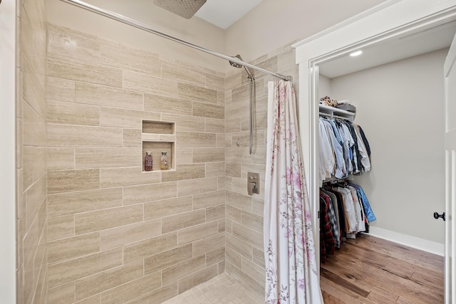 full bathroom with baseboards, a walk in closet, a stall shower, and wood finished floors