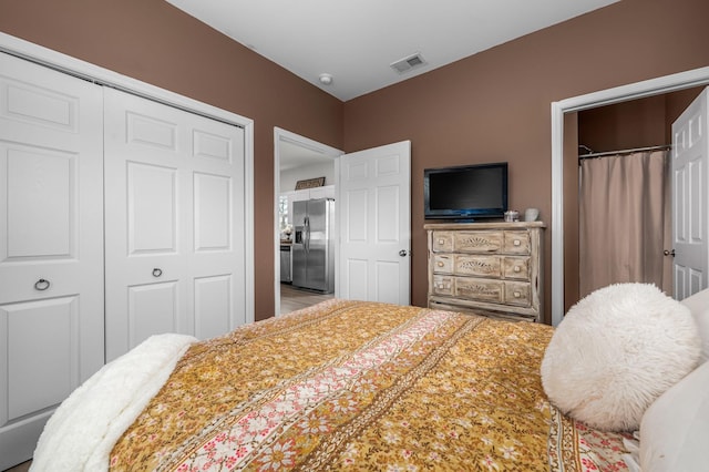 bedroom with a closet, visible vents, and stainless steel refrigerator with ice dispenser