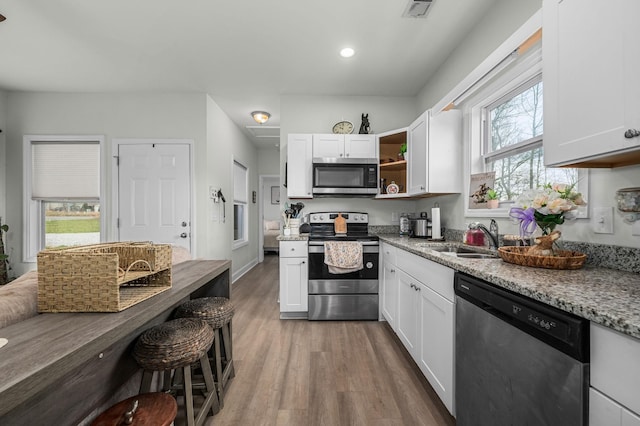 kitchen with a sink, light stone countertops, appliances with stainless steel finishes, and white cabinets