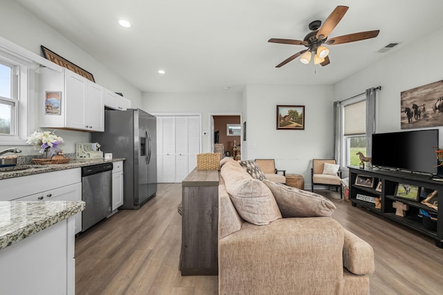 living area with light wood-style flooring, a ceiling fan, visible vents, and a wealth of natural light