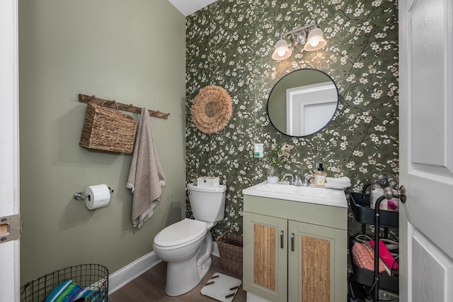 half bathroom featuring toilet, wood finished floors, wallpapered walls, baseboards, and vanity