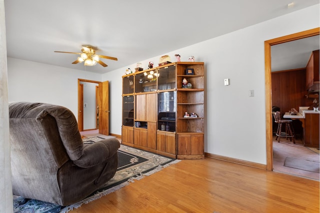 living area featuring baseboards, ceiling fan, and light wood finished floors