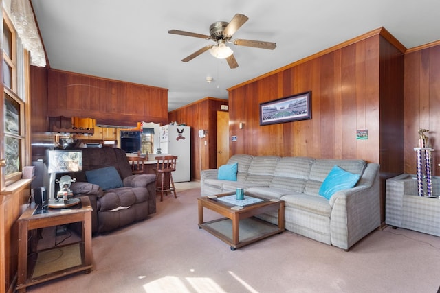 living area featuring wooden walls, light colored carpet, and a ceiling fan