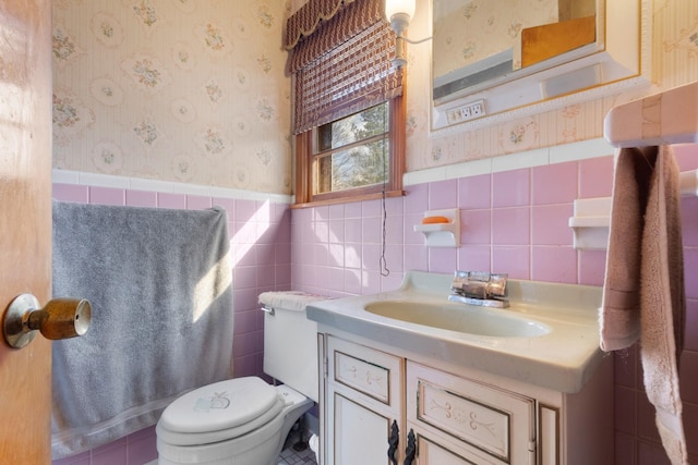 bathroom featuring vanity, toilet, wainscoting, and wallpapered walls