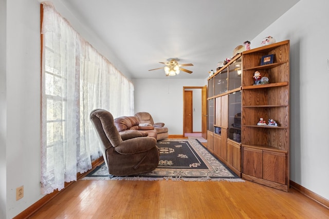 living room with baseboards, light wood-style floors, and a ceiling fan