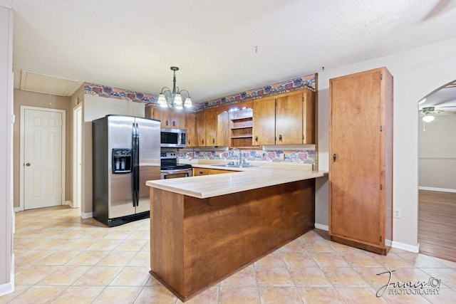 kitchen featuring brown cabinets, a sink, appliances with stainless steel finishes, a peninsula, and light countertops