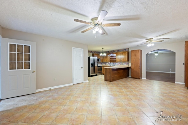 kitchen featuring a ceiling fan, brown cabinets, a peninsula, stainless steel appliances, and open floor plan