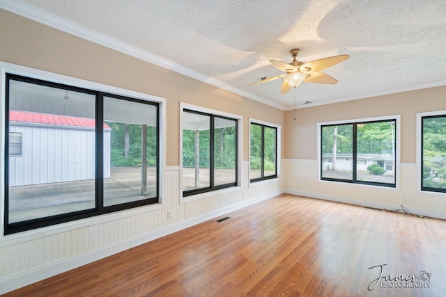 empty room featuring a wainscoted wall, a textured ceiling, a ceiling fan, and wood finished floors