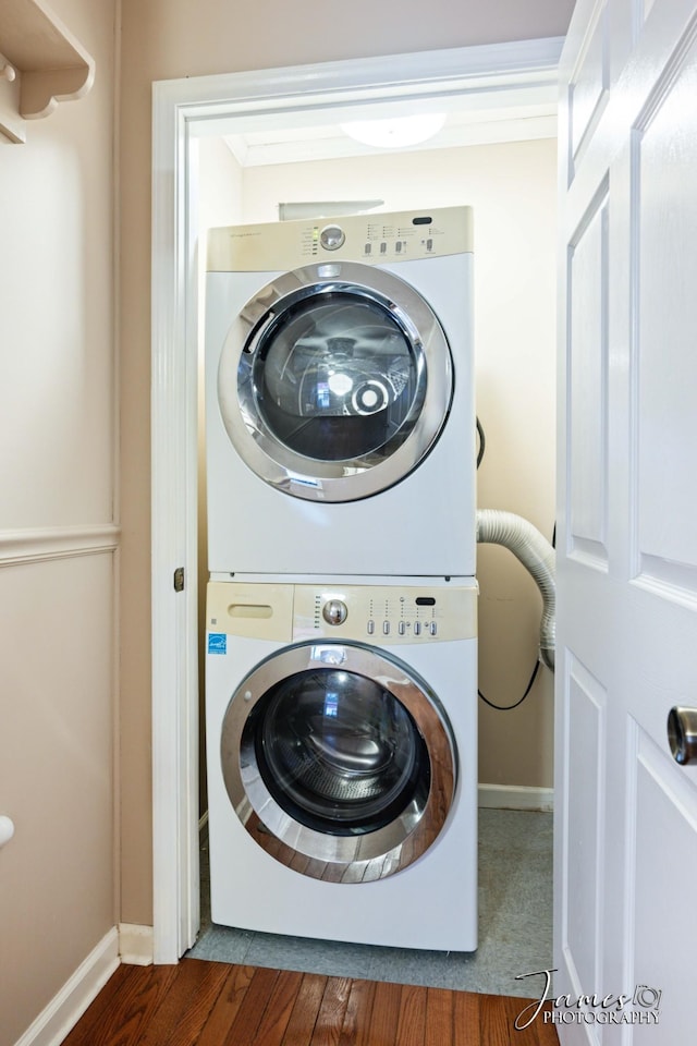 clothes washing area featuring laundry area, stacked washer / drying machine, baseboards, and wood finished floors