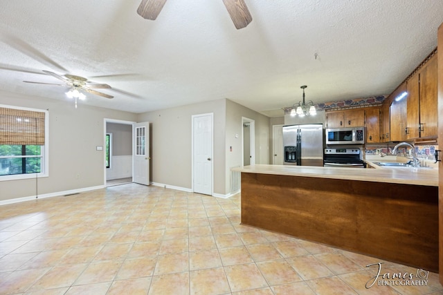 kitchen with brown cabinets, appliances with stainless steel finishes, light countertops, and ceiling fan with notable chandelier