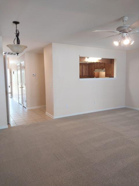 spare room featuring light colored carpet, ceiling fan, baseboards, and light tile patterned flooring