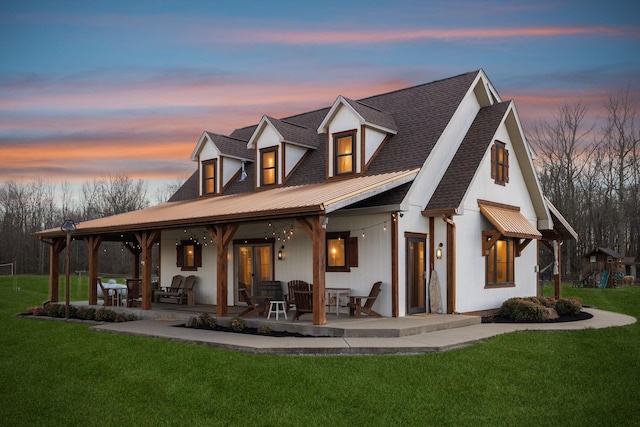 back of property at dusk with a patio, a lawn, and roof with shingles