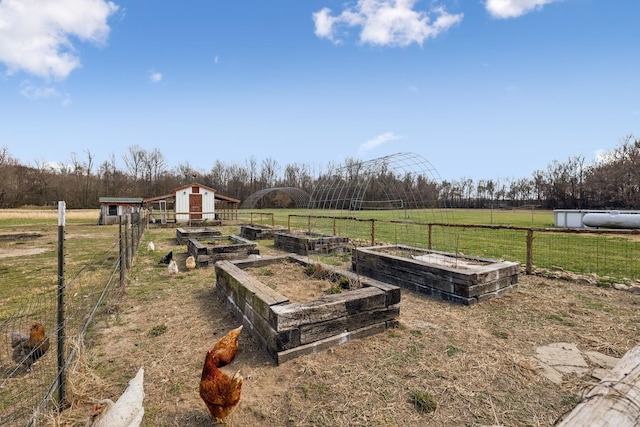 view of yard featuring a rural view, an outdoor structure, a vegetable garden, and fence