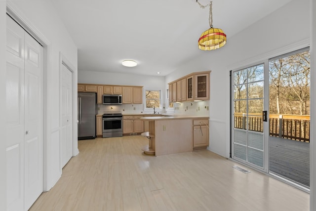 kitchen featuring glass insert cabinets, light brown cabinetry, light countertops, light wood-style flooring, and stainless steel appliances