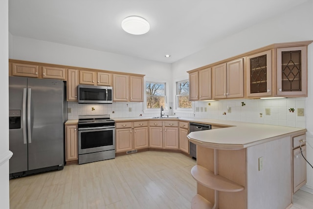 kitchen with a peninsula, stainless steel appliances, decorative backsplash, light countertops, and glass insert cabinets
