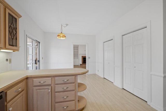 kitchen with a peninsula, a fireplace, light countertops, light wood-style floors, and backsplash