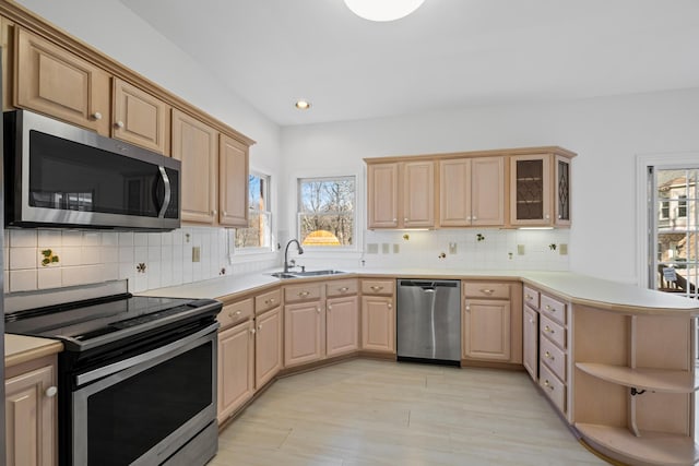 kitchen with a sink, a peninsula, light brown cabinetry, and stainless steel appliances