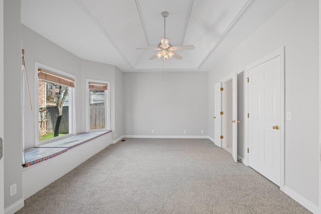 carpeted spare room featuring a tray ceiling, baseboards, and ceiling fan