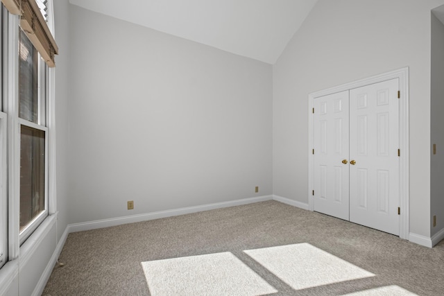 unfurnished bedroom featuring carpet, baseboards, a closet, and high vaulted ceiling