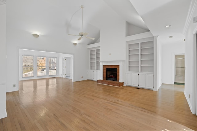 unfurnished living room featuring light wood-type flooring, high vaulted ceiling, a ceiling fan, built in features, and a brick fireplace