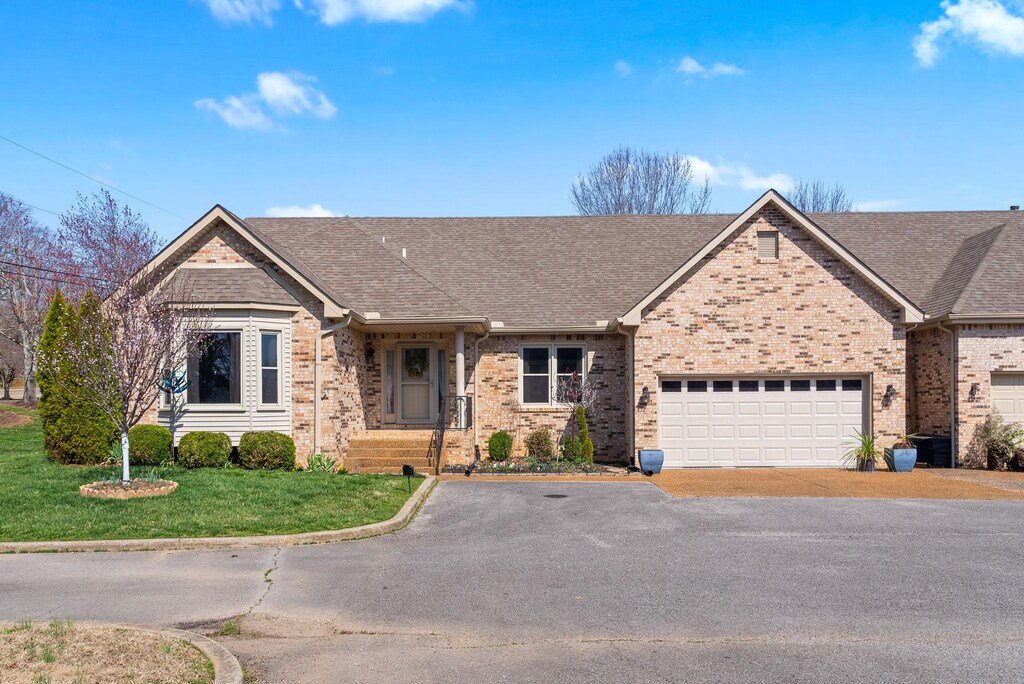 single story home featuring aphalt driveway, brick siding, a front yard, and roof with shingles