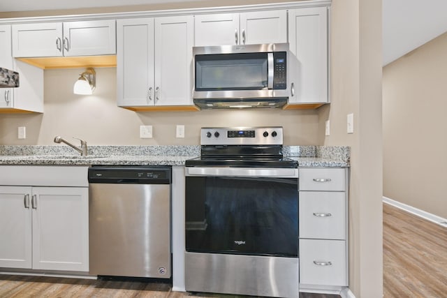 kitchen featuring appliances with stainless steel finishes, light wood-type flooring, and light stone countertops