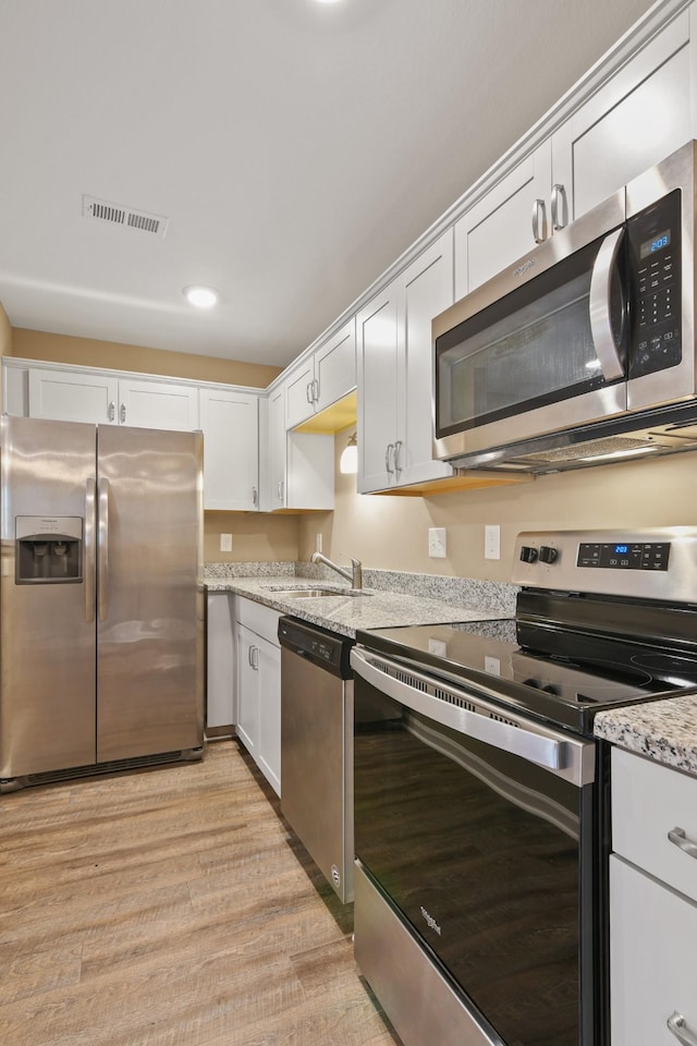 kitchen with visible vents, light wood-style flooring, a sink, white cabinetry, and stainless steel appliances