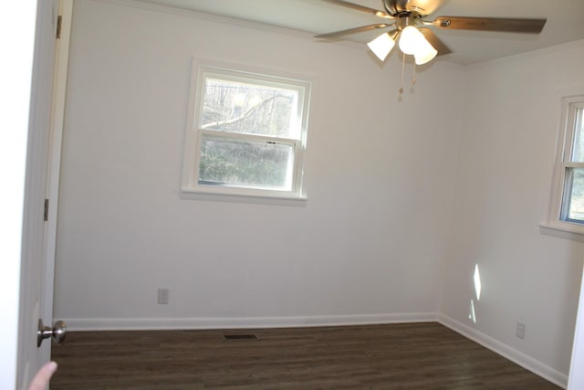 empty room with dark wood finished floors, visible vents, crown molding, and baseboards