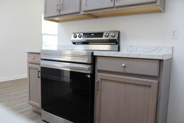 kitchen with stainless steel electric range oven, baseboards, light wood-style flooring, and light countertops