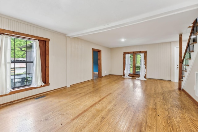 unfurnished living room with wood finished floors, a wealth of natural light, and stairs