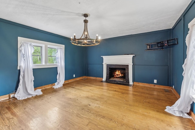 unfurnished living room with a fireplace, wood finished floors, baseboards, and an inviting chandelier