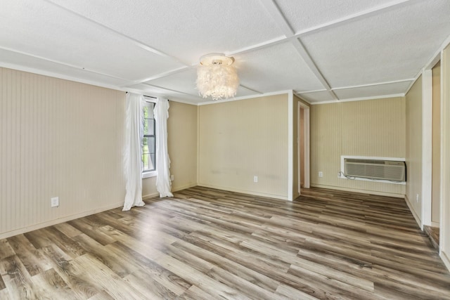 empty room featuring baseboards, wood finished floors, a wall mounted AC, and a textured ceiling