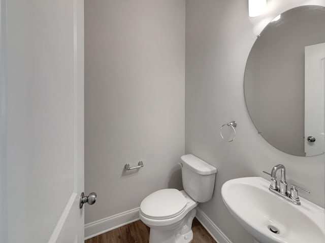 half bathroom with toilet, wood finished floors, baseboards, and a sink