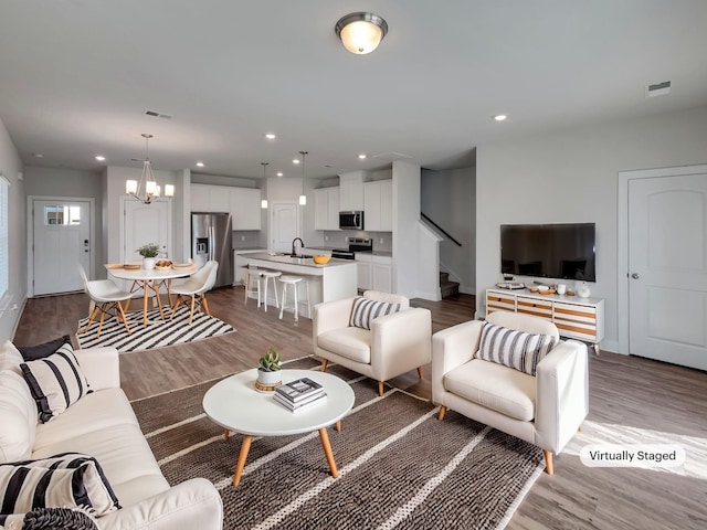 living area featuring visible vents, stairs, recessed lighting, an inviting chandelier, and wood finished floors