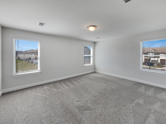 empty room featuring plenty of natural light, baseboards, visible vents, and carpet floors