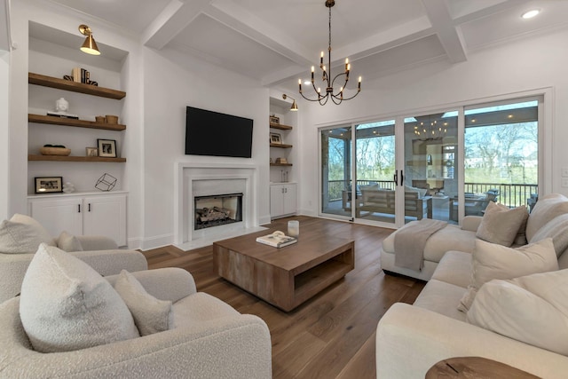 living room featuring coffered ceiling, dark wood-style floors, an inviting chandelier, a fireplace, and built in shelves