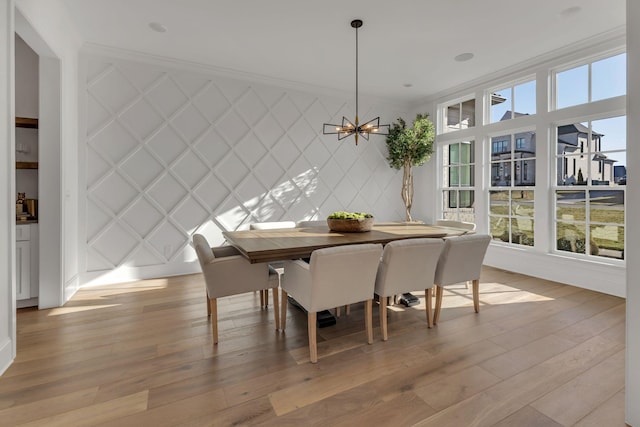 dining space featuring light wood-style floors, a notable chandelier, a decorative wall, baseboards, and ornamental molding
