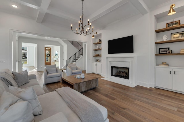 living area featuring a fireplace with flush hearth, beamed ceiling, stairway, wood finished floors, and built in features