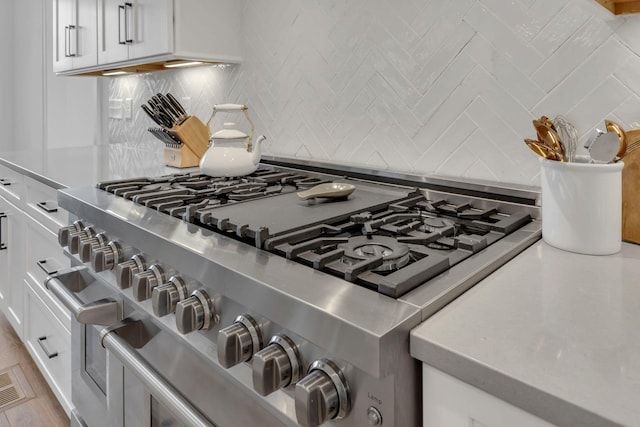 room details featuring light countertops, white cabinets, range with two ovens, and tasteful backsplash