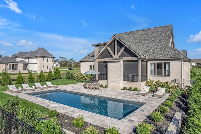 rear view of house featuring fence, a fenced in pool, a patio area, and brick siding