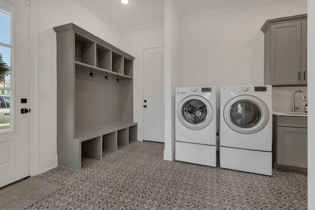 clothes washing area with cabinet space, ornamental molding, washing machine and dryer, baseboards, and a sink