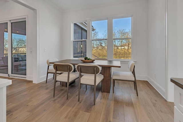 dining space featuring crown molding, light wood finished floors, and baseboards