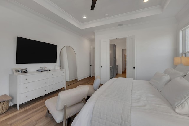 bedroom with crown molding, a raised ceiling, and light wood-type flooring