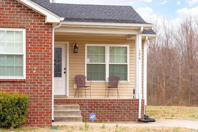 doorway to property featuring brick siding, a shingled roof, and covered porch